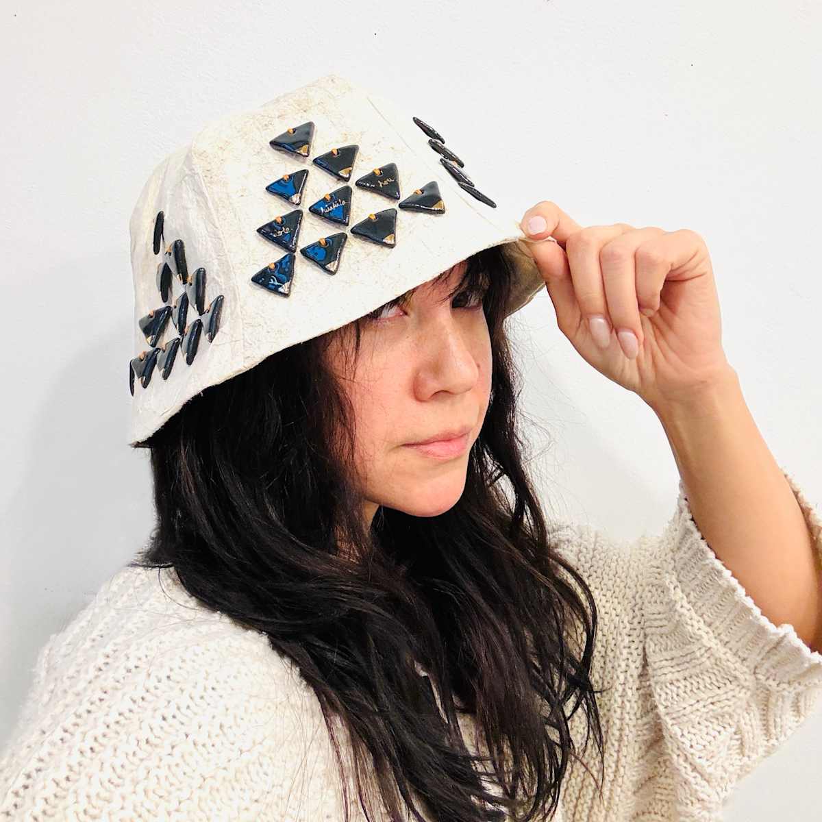 The Lone Wauke of Wakinekona. by Malia Peoples  Image: The Lone Wauke seeks to address questions of identity, authenticity, and provenance. Words on the hat are: “He kukāhi au, he wauke no Wakinekona. ‘Oia’i’o, lawa, ho’olōkahi. ‘A’ohe hilahila hou.” (I stand alone, I am the wauke of Washington. Authentic, enough, bringing unity. No more shame.)

This 6-paneled hat features kapa made in the traditional Hawaiian way from a mix of wauke (paper mulberry) grown in Hawaii and in Washington State and lined in cotton fabric. 60 individually formed charcoal porcelain tiles are fired with 18k gold and hand stitched with cotton thread. Tiles include handwritten prose in gold inspired by ʻŌlelo Noʻeau no. 708, The Lone Wauke of Kūloli (one who stands alone in their battles). Dimensions: 11” x 9” x 8”