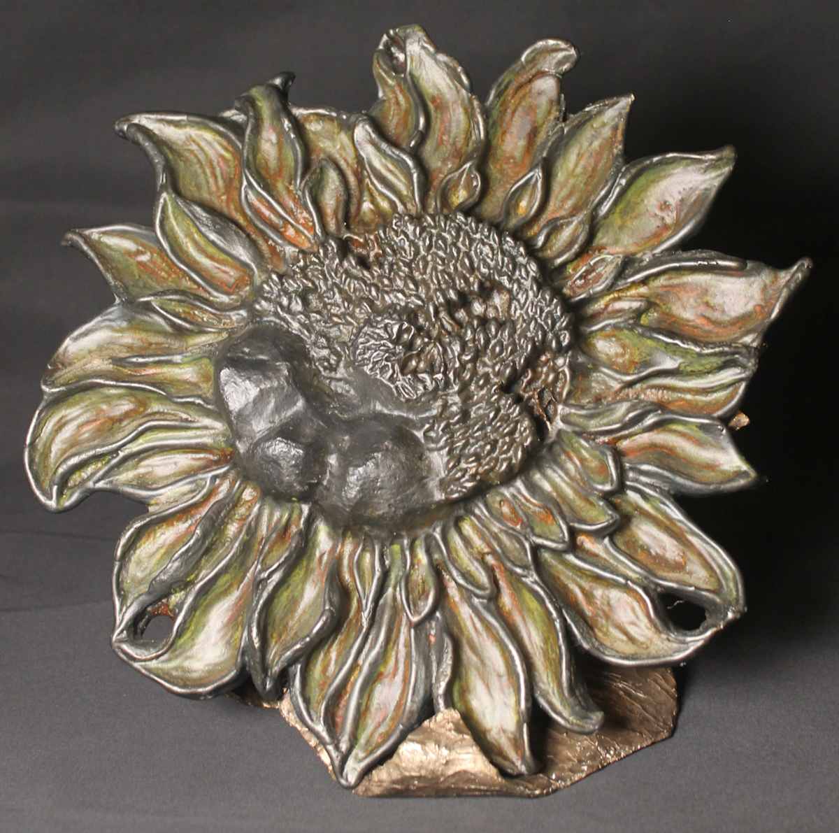 Sonjia by Jan Somers  Image: Sonjia is a tribute to the Ukraine.  The center represents the 3 mountain ranges of Ukraine, some of the seeds are missing, representative of the conflict. Sonjia means sunflower, the national flower of Ukraine, a symbol of peace and resilience. Sonjia is cast in Iron and then sits on a base created using the lost wax process, and cast in Bronze.  