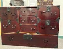 Trunk 001  Image: This object may be described as a trunk rather than a chest because it appears to have been designed for use on long trips away from home. The handles on either end, which may be raised up above the top of the trunk, allow for the insertion of a wooden plank or pole to enable two strong individuals to carry the piece. The lower drawer is decorated with floral motifs and the three drawers in the center would have been covered originally by a decorative wooden panel that could have been locked.