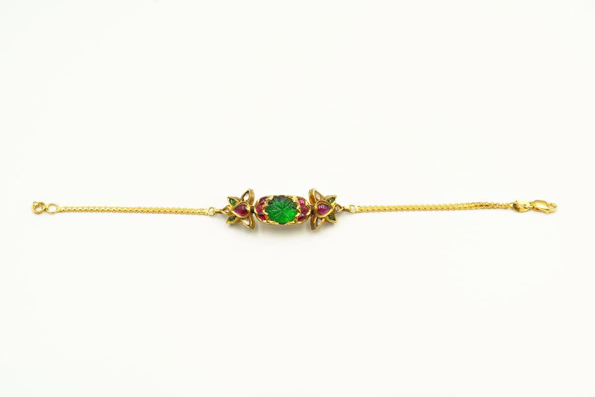 Pair of Bracelets  Image: Carved emeralds with blooming floral motifs form the centerpiece of these royal bracelets, framed by ruby-set poppy clusters with gold accents and flanked by slender twin gold chains.
