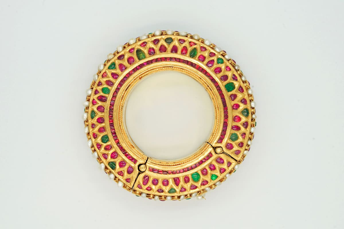 Gold bracelet  Image: This gold bracelet exemplifies the kundan technique, with rubies and emeralds set in an intricate lattice, edged with pearls. A hinged opening with clasp combines elegance with practicality.
