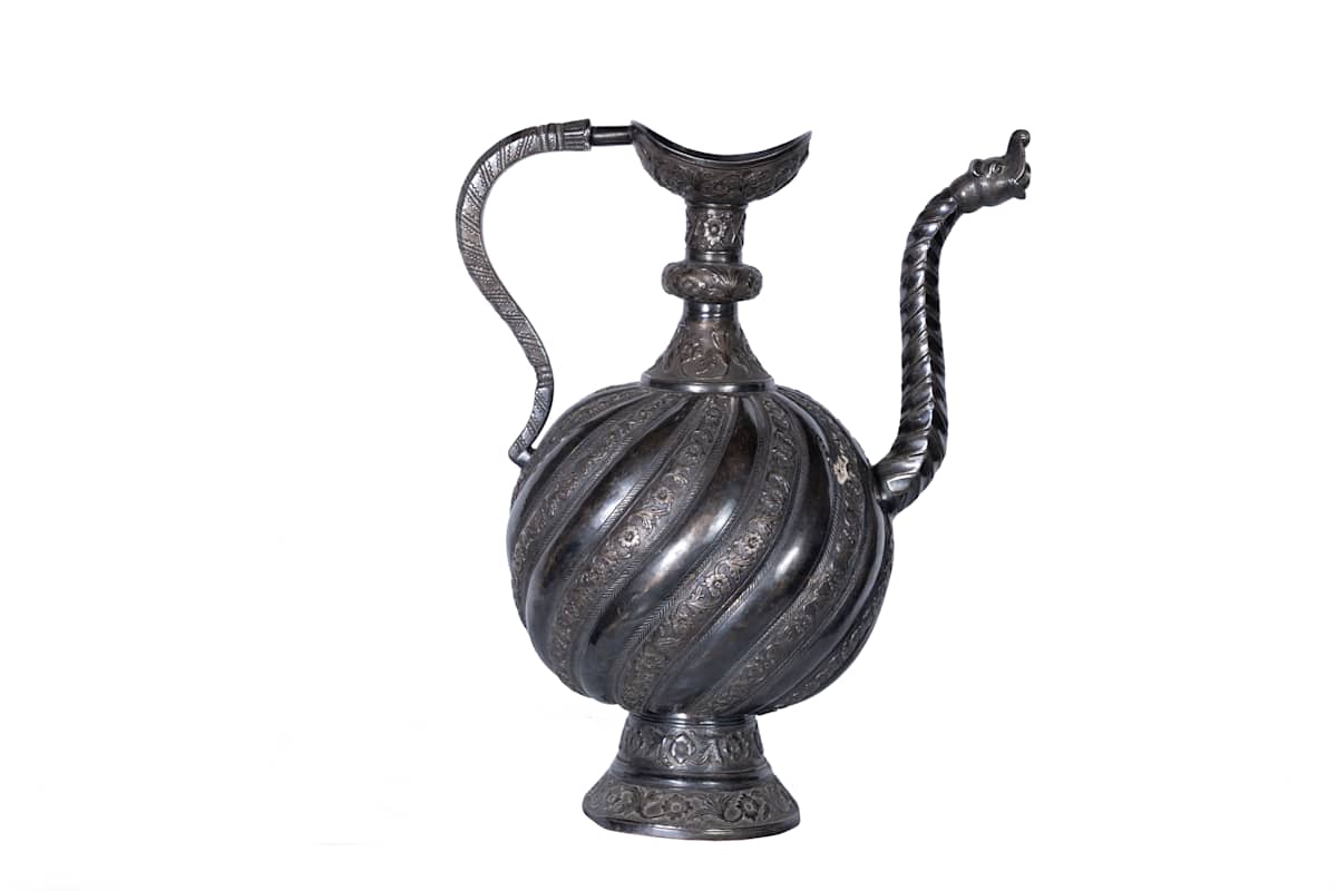 Ewer  Image: This silver ewer displays spiraling ribs, a makara spout, and floral engravings, culminating in a crescent-shaped mouth.
