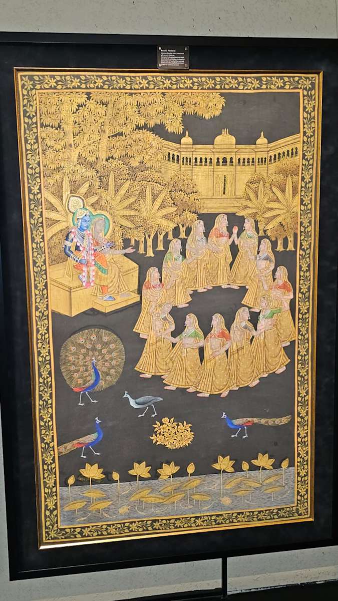 Rasalila Picchavai  Image: Surrounded by blooming lotuses and elegant peacocks, Radha and Krishna sit enthroned as gopis perform the Rasalila. A lush grove and ornate palace setting amplify the devotional spirit of this Nathdwara picchavai.