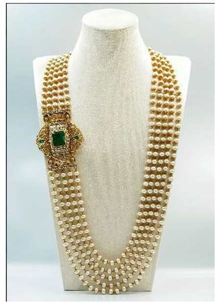 Gold Necklace  Image: This five-strand pearl necklace features an offset gold clasp set with emeralds in traditional kundan technique. Detailed with floral engravings and a central lion motif, it is finished with suspended gold bead tassels.