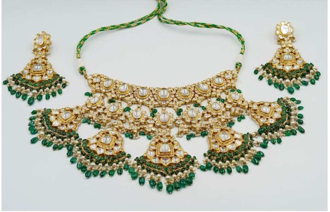 Gold Gem set Necklace and Earrings  Image: Rooted in regal traditions, this contemporary necklace set features crescent and floral motifs adorned with uncut polki diamonds. Handcrafted using age-old techniques, it is accented with cascading emerald beads and pearls. The matching earrings echo the design, evoking the grandeur of courtly elegance in a refined contemporary expression.
