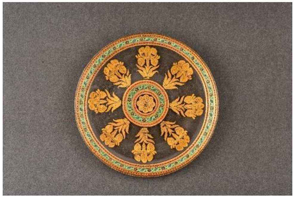 Mughal glass plate  Image: Free-blown and gilded, this Mughal glass plate features a central enamelled rosette and radiating floral motifs. Likely made in imperial workshops, it blends Persian design with European glassmaking, embodying courtly luxury and refinement.



