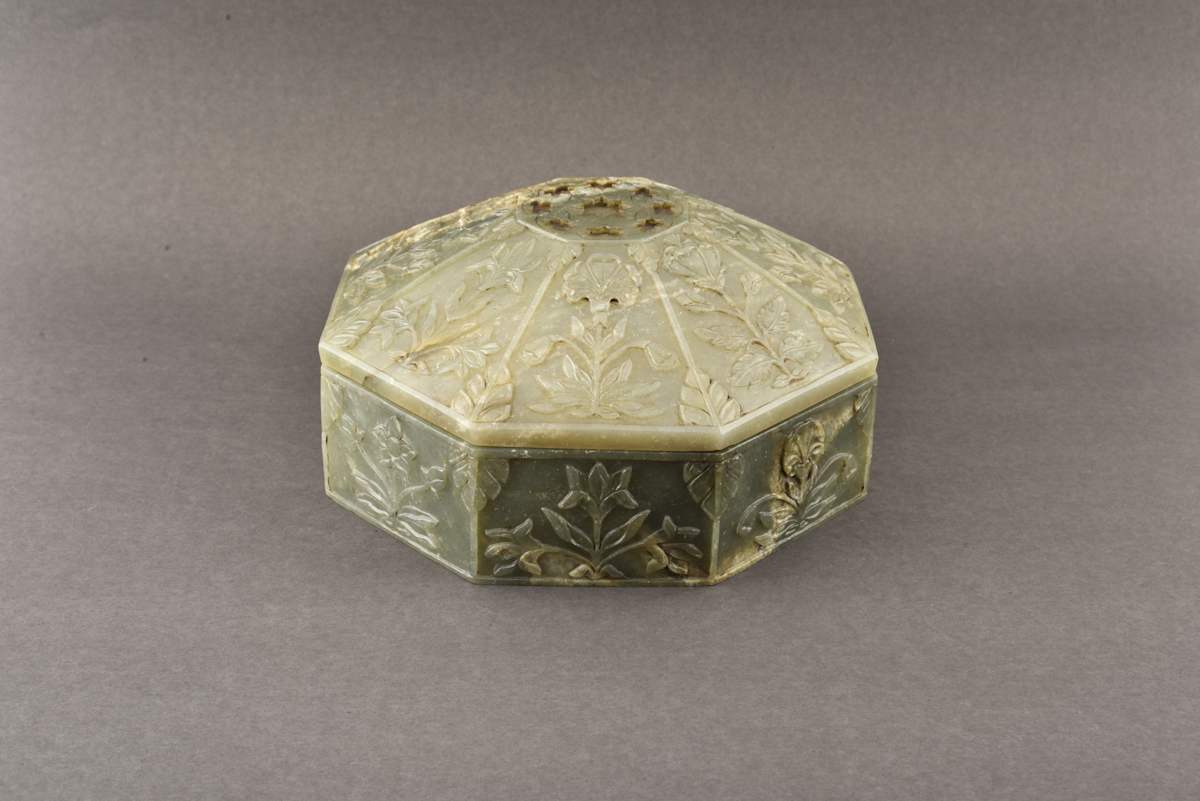 Octagonal box  Image: A masterpiece in Jade, this octagonal box gleams with carved floral panels and a radiant emerald-inlaid rosette. It reflects the refined elegance of Mughal decorative traditions in both form and detail.