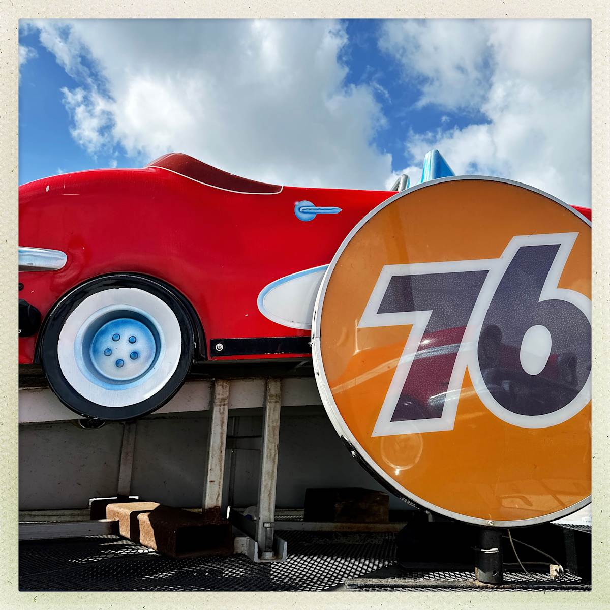 76 by Sherry Ross  Image: Wandering through a carnival in the process of being set up, I stumbled upon the familiar sight of little race cars, getting ready to spin endlessly in their neon-lit track—going nowhere, yet carrying memories in their loops. The chrome gleam of the ‘76’ gas logo catches flickering reflection of another tiny vehicle, a nostalgic beacon of roadside Americana. Behind it, a miniature red Corvette sits poised, frozen in time, its glossy curves promising the thrill of the open road within the confines of its small, circular world. The scene is both charming and bittersweet—a reminder that sometimes, the joy isn't in the destination, but in the ride itself.