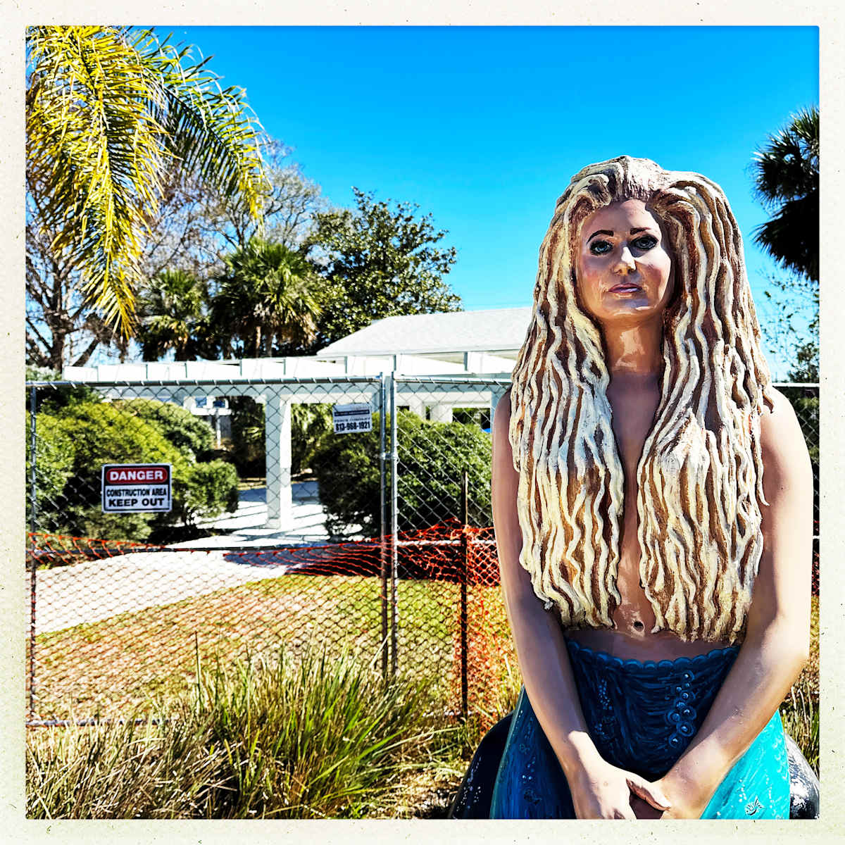 Danger Mermaid by Sherry Ross  Image: Weeki Wachee, one of Florida’s oldest amusement parks, carries with it the echoes of a bygone era. Though its days of grandeur have faded, visitors still gather for the mermaid shows—a charming relic of a simpler time. The magic lingers, even as the park itself wears the weight of years.

Amidst the quiet decay, a vintage mermaid statue stands frozen in time. Her expression, once vibrant, now bears the layers of countless seasons—paint peeling, then repainted, only to peel again. She is a silent witness to the park’s past splendor, a symbol of nostalgia and resilience even as she presides over the renovations. Though weathered, she remains, much like Weeki Wachee itself—fading, yet never forgotten.