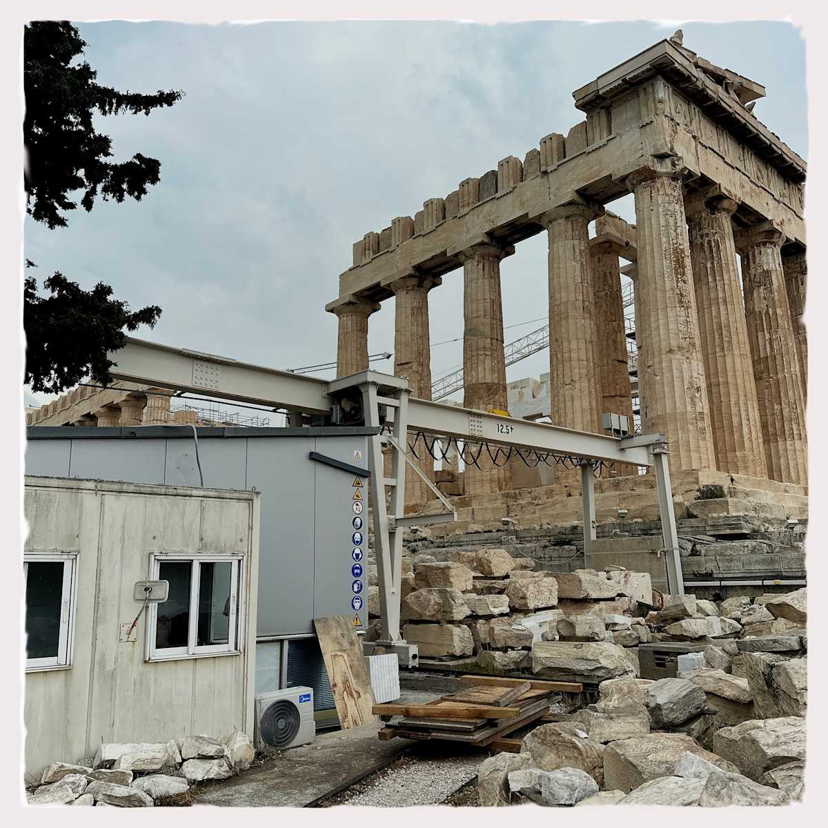 DIY Home Improvement by Sherry Ross  Image: The ongoing restoration of the Greek Acropolis feels like an eternal DIY project—centuries of missing pieces stolen or eroded, leaving history in a constant state of repair. Scaffolding clings to the ancient stones, a modern intervention against the slow decay of time. Amidst this grandeur, a ramshackle construction shanty stands in jarring contrast, its weathered boards and temporary presence underscoring the absurdity of the scene. The Acropolis, a symbol of timeless civilization, now shares space with the fleeting and the makeshift—a reminder that even the most enduring legacies require patchwork and persistence to survive.