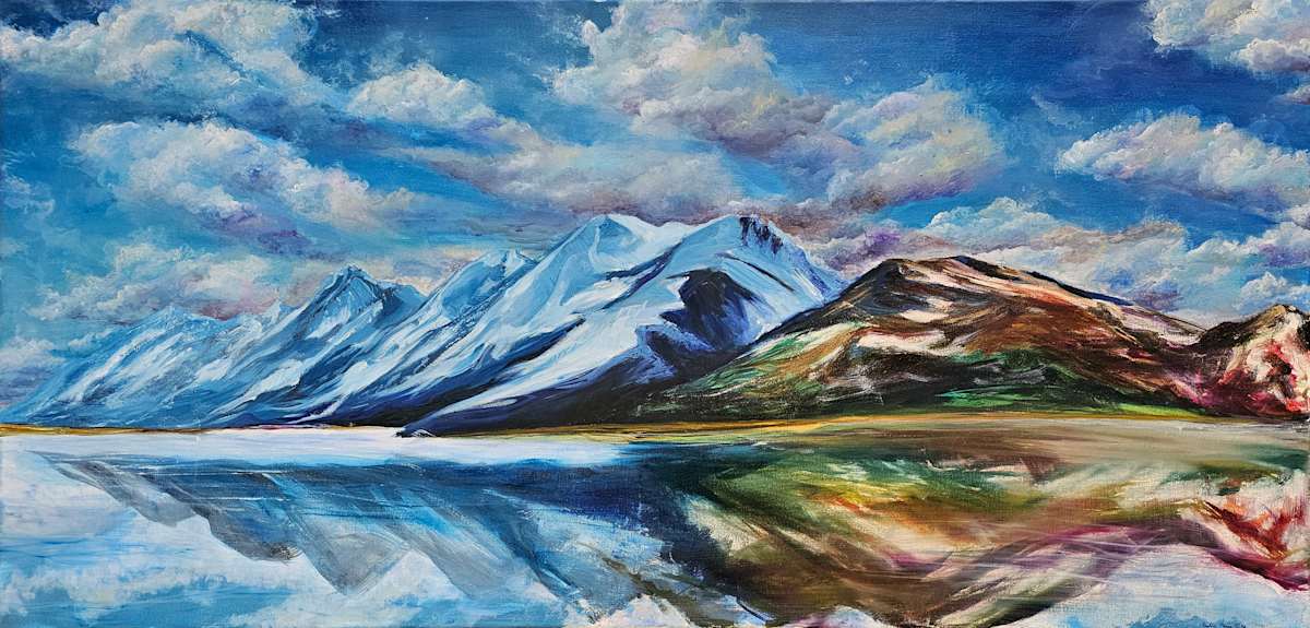 Amid The Blue by Tashina Marie  Image: A crystal-clear lake in the Grand Tetons National Park, reflects the brilliant blues of an early spring sky. Snowy mountains also appear blue with the vibrant sky. Amid this vast panorama of azure, a lone peak erupts in a burst of Spring color.