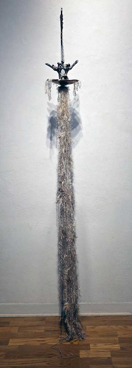 Memento Mori by Tashina Marie  Image: This memento mori sculpture is a meditation on life, death, and the unseen threads that connect all existence. At its core, a back vertebrae cast in aluminum serves as the structure of the piece—symbolizing the conduit of life’s energy, the spine that carries the electrical impulses animating the body. Delicate mushrooms emerge from its surface, a reminder of nature’s cycle of decay and renewal.
Within the hollow center of the vertebrae, a spider is cut out, embodying the weaver of fate—spinning the narratives of life and guiding souls toward the unknown. Beneath this, a shallow, hammered copper bowl cradles the fragile wings of a death moth, a creature drawn to the light, embodying both transformation and the inevitability of passing.
Spilling from the bowl, delicate tendrils of mycelium spread outward—an intricate network mirroring the nervous system, the unseen web that connects all living things, whispering signals across the earth. Dandelion seeds dust the entire composition, carrying the ephemeral nature of existence. They remind us that life, like the fleeting wish of a child blowing seeds into the wind, is precious while it blooms—not only in its final moments. This sculpture invites reflection on the beauty of impermanence and the interconnectedness of all things.