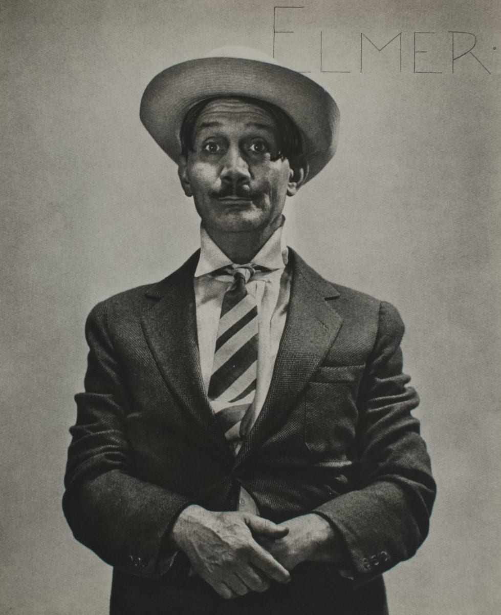 Elmer by Shirley Hall  Image: A black and white portrait of a mustached man in suit and tie. His hands are crossed and held in front of his stomach. In the top right there is the word "ELMER", presumably the subject's name. 