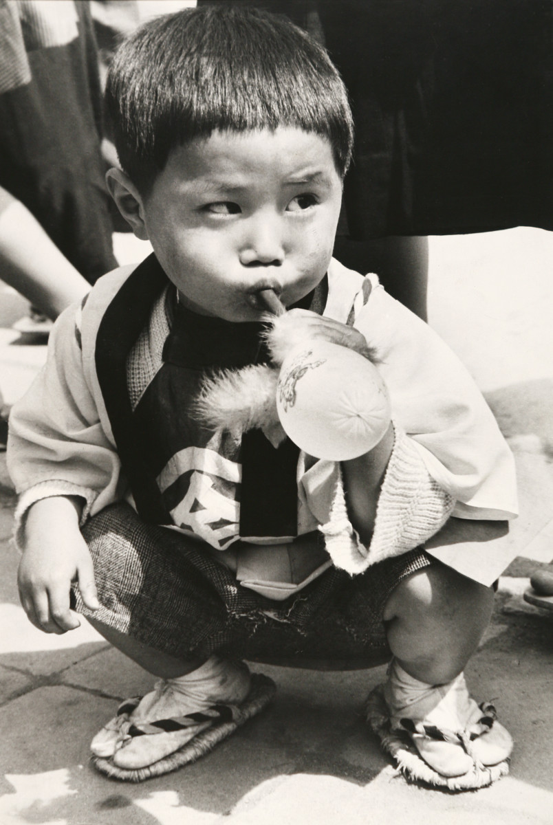 Untitled by Edward R. Miller  Image: A young Asian child crouching and blowing air into a balloon 