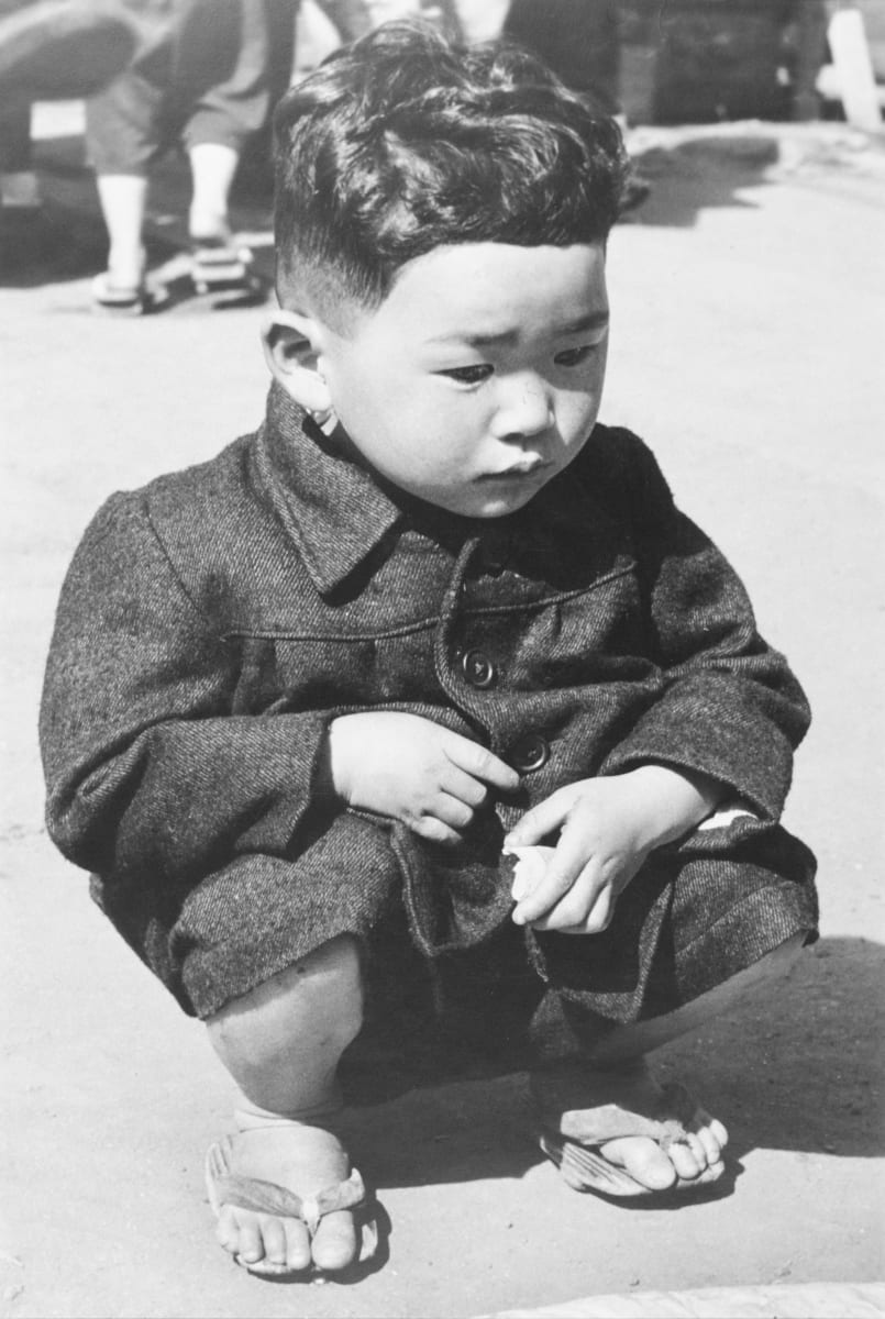Children of Today, Tokyo- Japan; Osaka, Japan 1948 by Edward R. Miller  Image: Small Asian child crouching in overcoat and thong sandals.