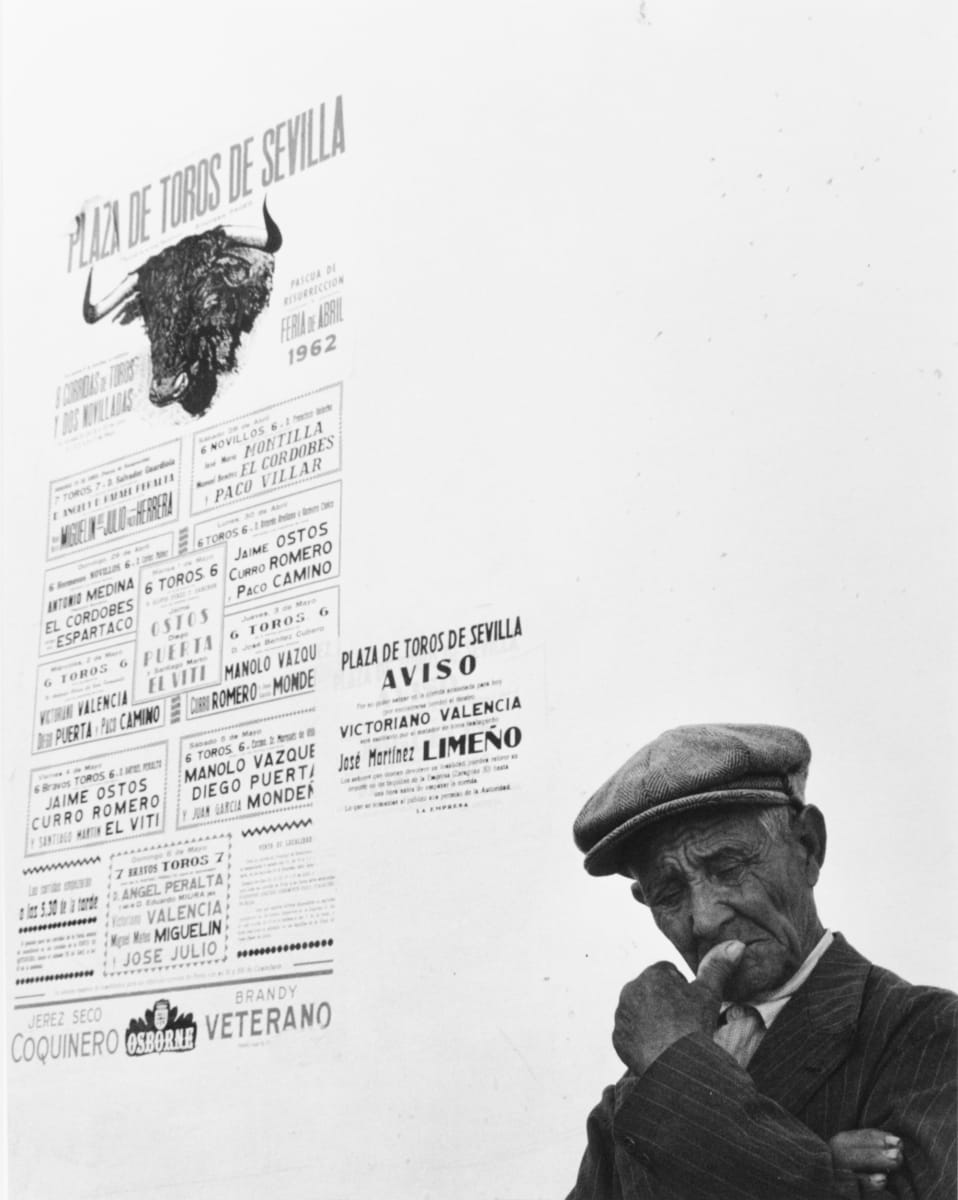Seville Spain 1962 by Edward R. Miller  Image: Tanned person in cap in front of a bull fighting poster written in Spanish.