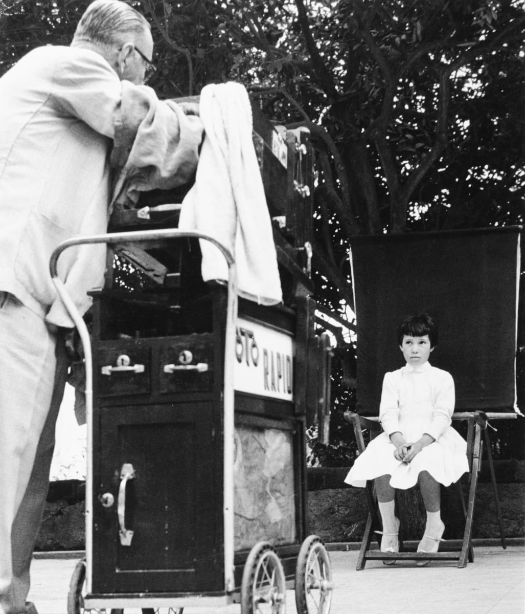 Canary Island, 1962 Photographer and Little Girl by Edward R. Miller  Image: A black and white photograph of a young girl being professionally photographed in a park.