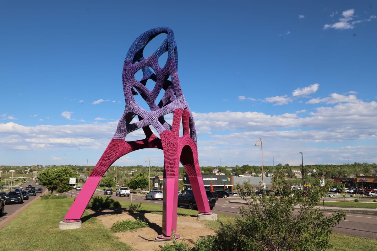 Tall, colorful abstract sculpture on a green median.