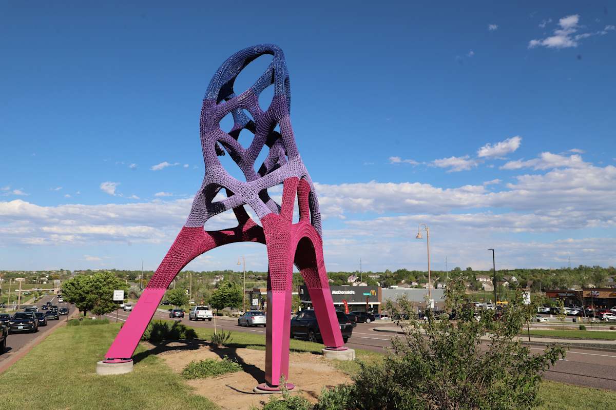 Tall, colorful abstract sculpture on a green median.