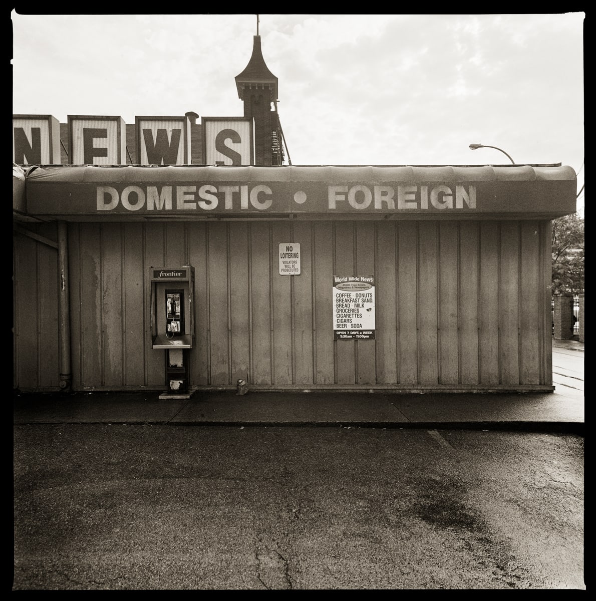 585.232.9376 – World Wide News, 100 Saint Paul Street, Rochester, NY 14604 by Eric T. Kunsman  Image: ID: A black and white image shows a building with signs for News Domestic and Foreign.  Under the signage on the overhang there is a payphone.