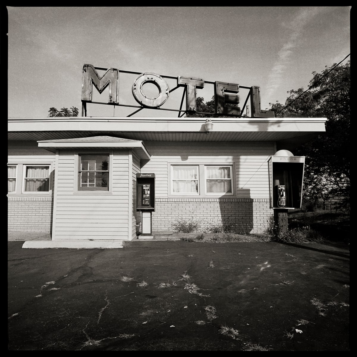585.235.9340 & 585.235.9923 – 490 Motel, 360 Mount Read Boulevard Rochester, NY 14611 by Eric T. Kunsman  Image: ID: A black and white image shows two payphones against a motel building.  One in mounted to the center of the building and the other is on a pole to the right of the building.  There is a large "Motel" sign on the roof of the building.