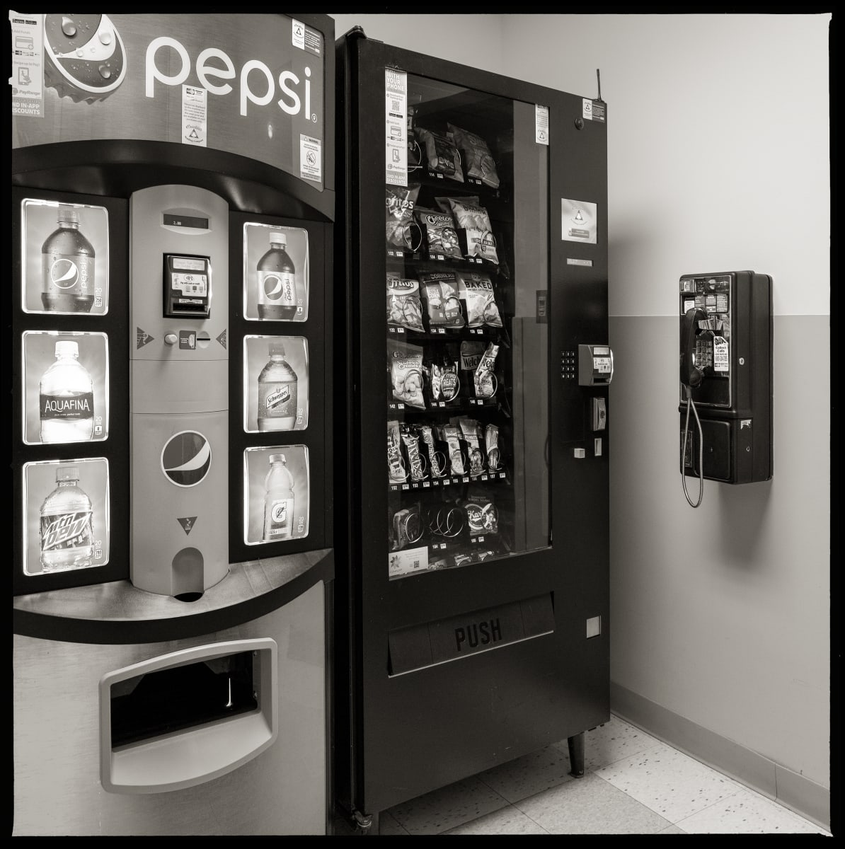 585.266.9430 – RGH Hospital, 1425 Portland Avenue, Rochester, NY 14621 by Eric T. Kunsman  Image: ID: A black and white image shows a wall mounted payphone to the right.  Against the left side wall of the corner are two vending machines- a Pepsi machine and a snack machine.