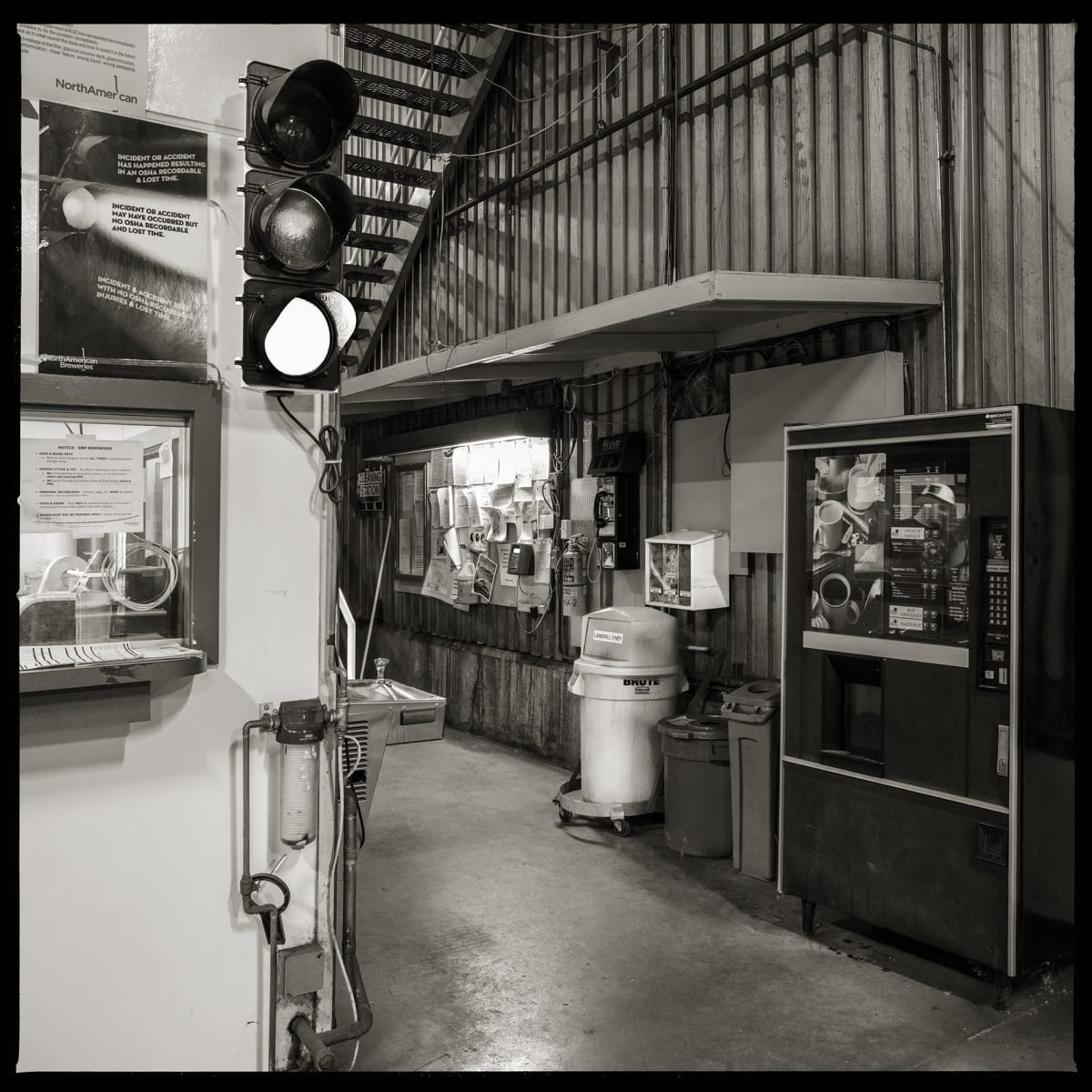 585.325.9325 – High Falls Brewing Company, 445 Saint Paul Street, Building #14, Rochester, NY 14605 by Eric T. Kunsman  Image: ID: A black and white image shows a door way room with a vending machine to the right and a window to the left.  There is a stoplight on the entrance way and a payphone between the window and vending machine.