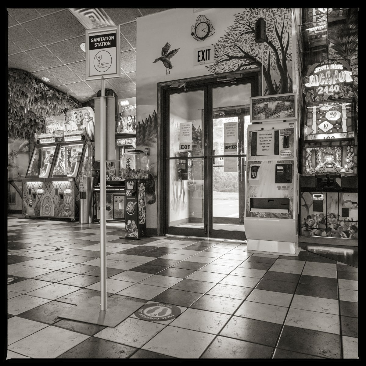 585.427.9535 – Clubhouse Fun Center, 70 Jay Scutti Boulevard, Henrietta, NY, 14623 by Eric T. Kunsman  Image: ID: A black and white image shows a glass door, where through the door there is a payphone on the left wall.  On the inner side of the door there are various game machines and a pattern tiled floor.
