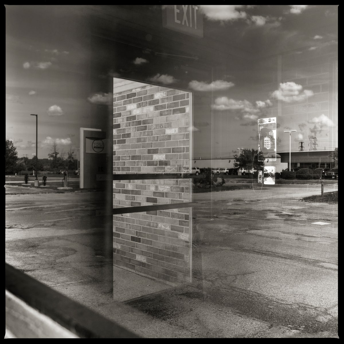 585.427.9821 – Pizza Hut #606105, 3120 Winton Road South, Rochester, NY 14623 by Eric T. Kunsman  Image: ID: A black and white image shows a semi-reflective window.  Though the reflection of the sky and the outside, there is a payphone in the building.  There is also a glass door that can be seen through the window in which there are bricks visible.