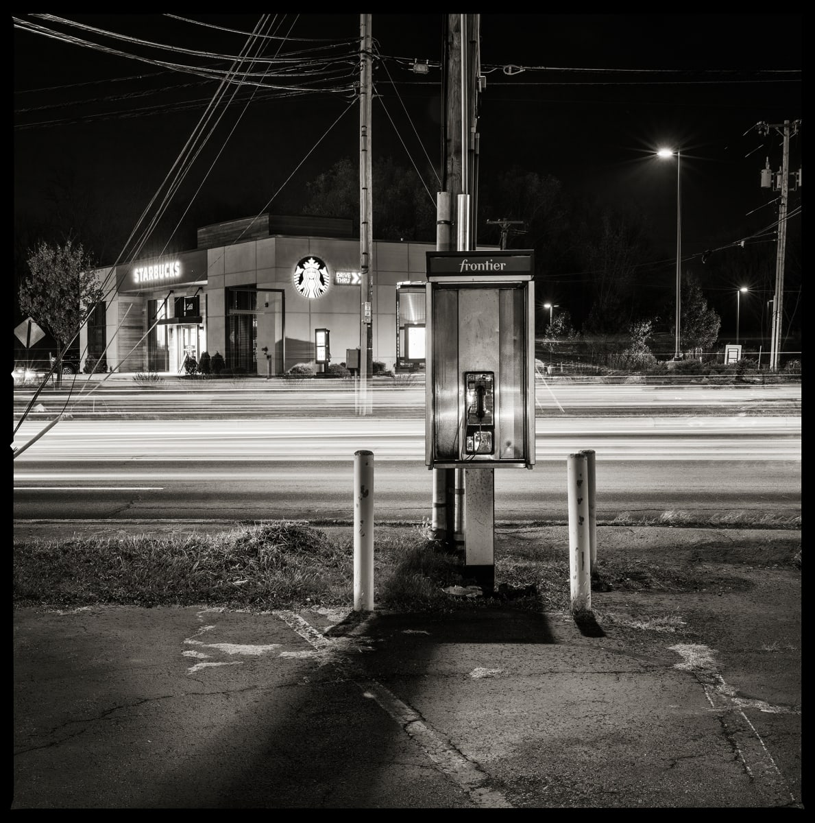 585.427.9848 – Stoney’s Plaza, 2852 West Henrietta Road, Henrietta, NY 14623 by Eric T. Kunsman  Image: ID: A black and white image shows a payphone against a telephone pole.  Behind the payphone is a Starbucks.