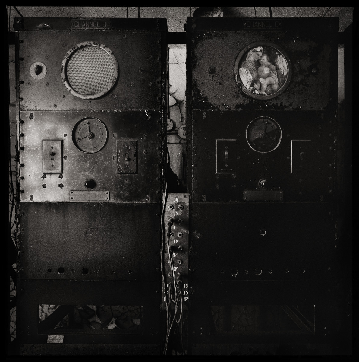 Religion Radio by Eric T. Kunsman  Image: ID: A black and white image shows two metal rectangles side by side.  They each have two circles, the bottom of which is a dial.  The top circle on the right machine have a picture of a religious figurehead.
