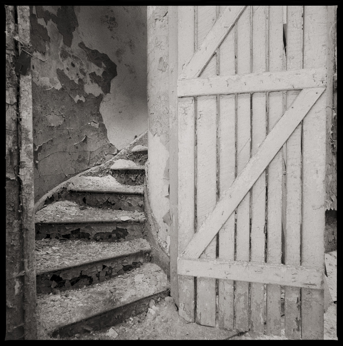 Untitled by Eric T. Kunsman  Image: ID: A black and white image shows a stairway leading upwards.  There is a wooden door to the right.  The stairs are covered in dust and debris.  
