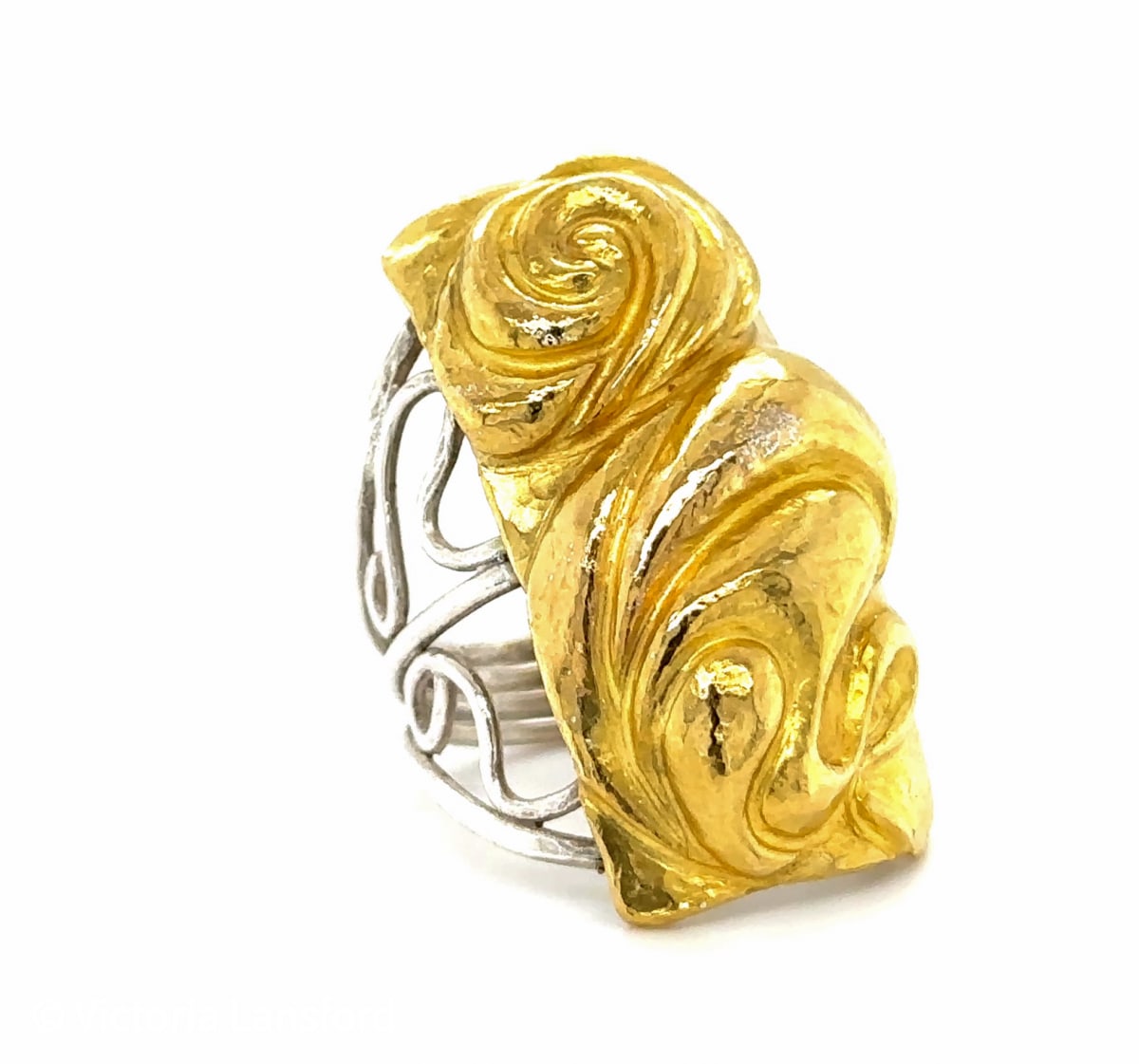 Rose Nouveau by Victoria Lansford  Image: Swirling petal forms wrap the finger to conjure the depth of a rose and the feel of La Belle Époque. This Eastern repoussé and scrollworked ring is free-hand forged from 18 karat gold sheet fused to a sterling silver backing, providing the warm color of gold with the lightness and stability of sterling in the lacy shank and beneath the relief work.