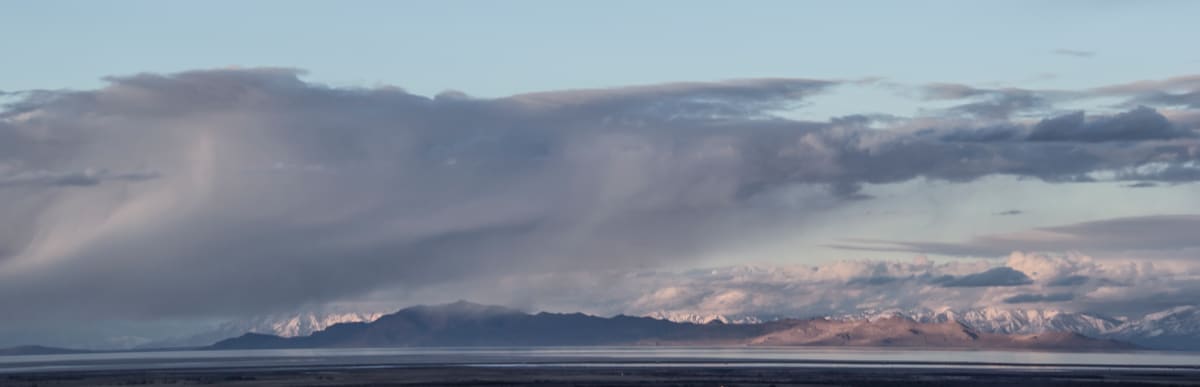 Panoramic Vista by Nila Jane Autry  Image: Photo taken with fully extended telephoto lens look across the distance from Grantsville Reservoir over the Great Salt Lake looking toward Salt Lake City.  The Skies were playful and joyous, making this the best photo op ever!  But it was Cold!!!