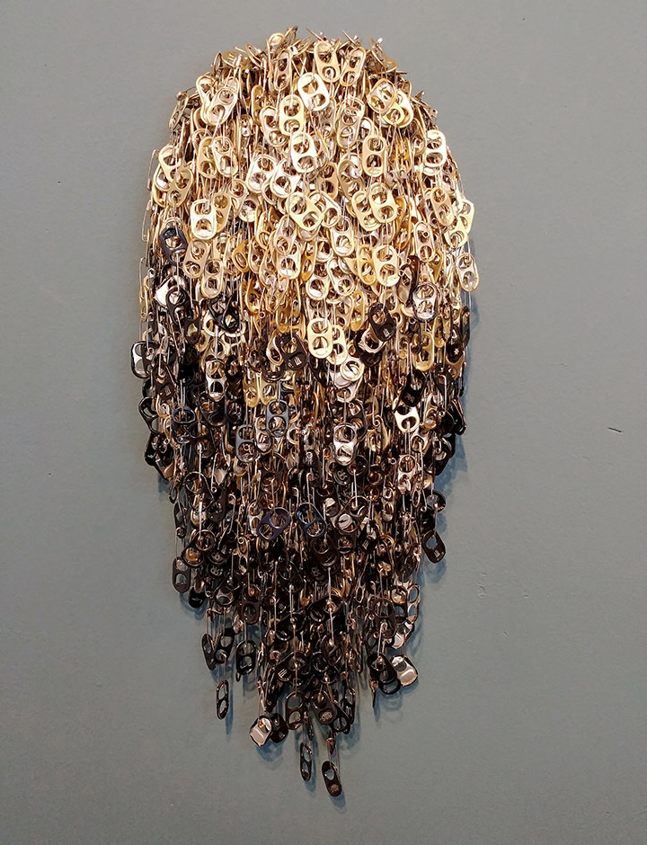 Treasure 6.8 (singed, gold with black lower 2/3rd) by Virginia Fleck  Image: About Treasure Series : Aluminum can-tabs chained together with safety pins are layered, massed and attached to an MDF backing creating a dense sparkling texture. The can-tabs are reflective, glinting in the light, catching the eye of those who pass by them. These shield-like, glittering wall pieces have the presence of valuable treasure, but closer inspection reveals that the treasure is made from can-tabs, one of many common disposable items that continuously pass through our hands. Hangs flush to wall on meatal cleat (included)
