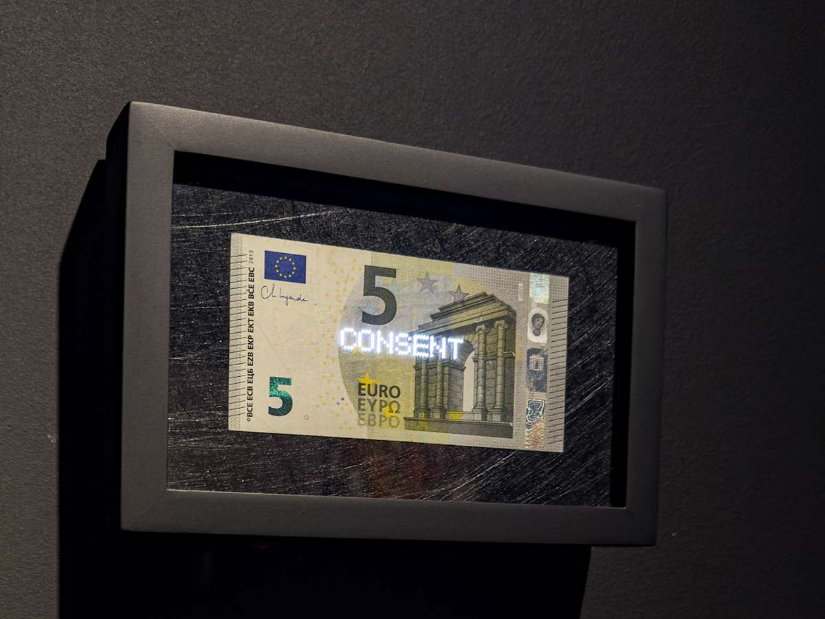 Planetary Values- 5 Euro Bill - Consent by Jorge Luis Vaca Forero  Image: Planetary Values- 5  Euro Bill / (Consent) is a unique approach to global politics. It focuses on the Euro bill, one of the main currencies in the world economy. This project highlights the most frequently mentioned values from the European Union’s Constitution by using laser cuttings to create perforations in the bills, which are then illuminated by LED lights.

The aim is to challenge the legitimacy and symbolic significance of the State. It does this by connecting the symbolism of money with the economy it represents and the values and commitments made by governments that are often not met around the world. The words on the bills can only be seen when illuminated, emphasizing their hidden nature.

This initiative turns these bills into seemingly useless objects and invites us to reconsider the global significance of currency. It questions the ideals of peace, well-being, and democracy that nations claim to uphold for their citizens, suggesting that these ideals may not be fully realized and are limited by the currency that represents economic and social exchanges.
