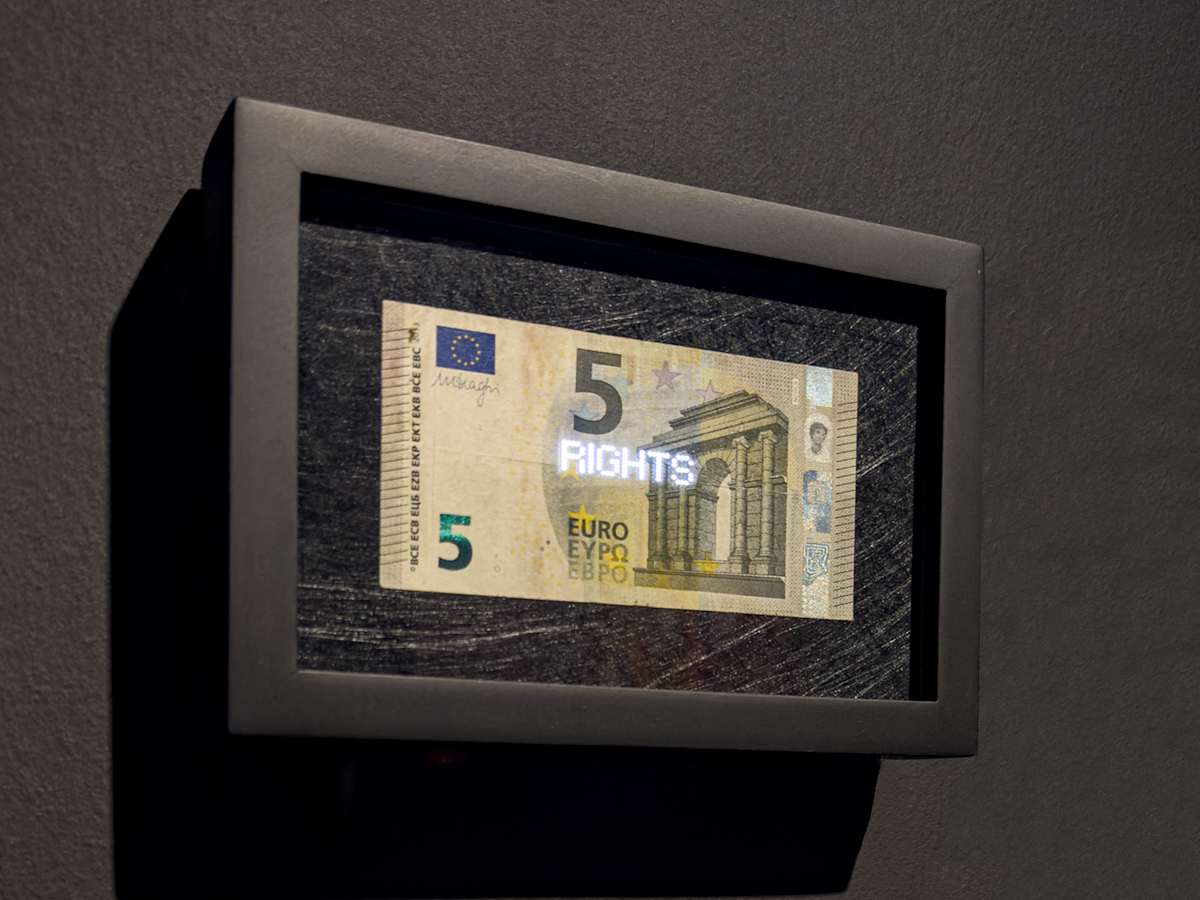 Planetary Values- 5 Euro Bill - Rights by Jorge Luis Vaca Forero  Image: Planetary Values- 5  Euro Bill / (Rights) is a unique approach to global politics. It focuses on the Euro bill, one of the main currencies in the world economy. This project highlights the most frequently mentioned values from the European Union’s Constitution by using laser cuttings to create perforations in the bills, which are then illuminated by LED lights.

The aim is to challenge the legitimacy and symbolic significance of the State. It does this by connecting the symbolism of money with the economy it represents and the values and commitments made by governments that are often not met around the world. The words on the bills can only be seen when illuminated, emphasizing their hidden nature.

This initiative turns these bills into seemingly useless objects and invites us to reconsider the global significance of currency. It questions the ideals of peace, well-being, and democracy that nations claim to uphold for their citizens, suggesting that these ideals may not be fully realized and are limited by the currency that represents economic and social exchanges.

