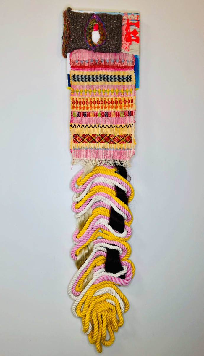 Tejido play by Katie Ruiz  Image: This is the first weaving I created on a back strap loom in Oaxaca. I was taught by a Zapotec woman in the mountains of Oaxaca. When I came home I used fake hair from my bridal makeup and hair kit and braided it with pink and yellow rope. Hair extensions are an important part of culture and this hair is blonde and brown showing my mixed race in the work. 