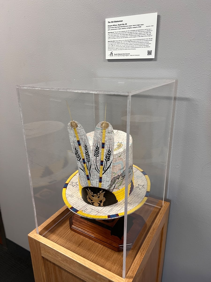 The Old Statesman by Dwayne Wilcox  Image: “The arts help to grapple with life’s challenges and celebrations, and for me, a way to reconnect with my community when I was away from home. This top hat is a reflection of a man held in high esteem. The antique paper highlights the state’s relation to the piece. The dragonfly design in copper is for Lakota culture ‘to see the truth though the illusion.’ The state seal is on the back of the hat near the feathers, and the copper is in the shape of the rising sun.”