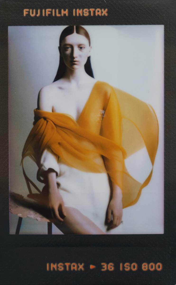 Sunward Shell / Containment Icon by Maria Lankina  Image: A vertical figure wrapped in a pale shell-like form stands inside a narrow column of light, held in place like a contained sunrise.