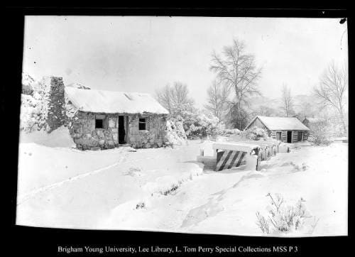 [Across Chalk Creek, Bridge Below Ledge on Main Street, Coalville] by George Beard  Image: A stone house and a wooden house, along a road, covered in snow.