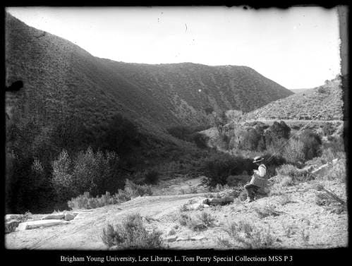 ["Narrows" on Chalk Creek ] by George Beard  Image: A person with fishing poles sits on a hillside, looking into a valley.