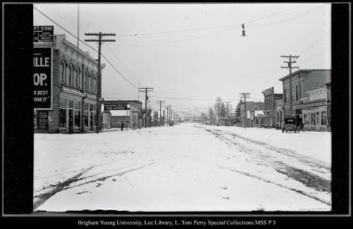 [A "Modern" Coalville with the electric poles in the middle of the street forced out by automobiles, two street lights, unpaved road] by George Beard  Image: A few cars on a snow-covered city street, electric poles.