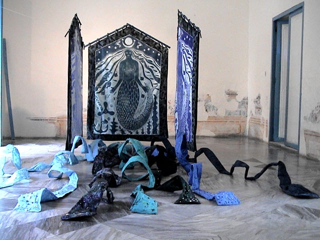 Yemaya Installation (Las ,muchas caras de Yemaya y la casa de Yemaya) by Imna Arroyo  Image: The House of Yemaya / La Casa de Yemaya, 2006; Woodcut prints on satin fabric, framed with Indonesian batik cloth;   78  x 52 x 96” 
