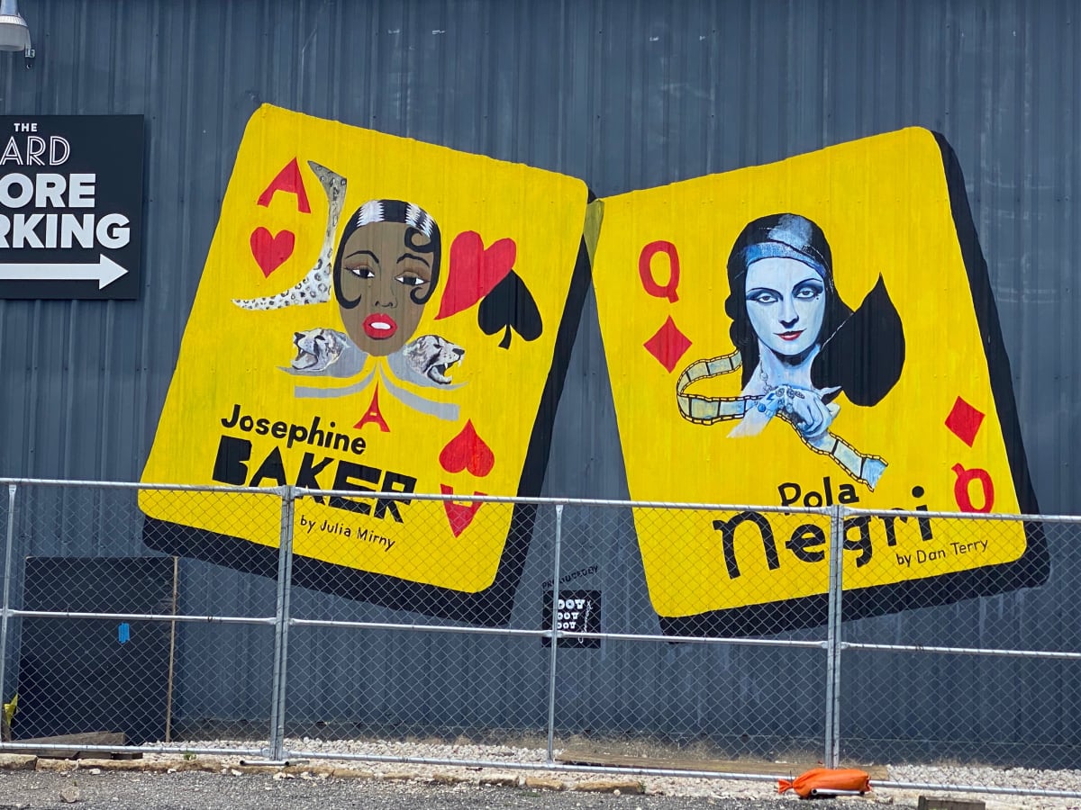 Polish Celebrities Playing Cards mural by Dan Terry  Image: This commissioned work of two famous celebrities celebrated by the Polish American community at Dot,Dot.dot.com is located just behind the Tesla showroom at the Yard on Industrial Drive in South Austin. Featured are Polish early film actress Pola Negre, who's affairs with Charlie Chaplin and Rudolph Valentino are legendary. Josephine Baker, American born black singer, is also shown as her popularity in Europe in both Paris and Poland far exceeded her success in the US. The card  of the Baker portrait was designed by Polish Artist Julie Mirney. The murals which measure approximately 10'x12' were painted by Dan Terry and regular assistant Danielle Villerreal over two weeks during a very rainy May in 2021. 