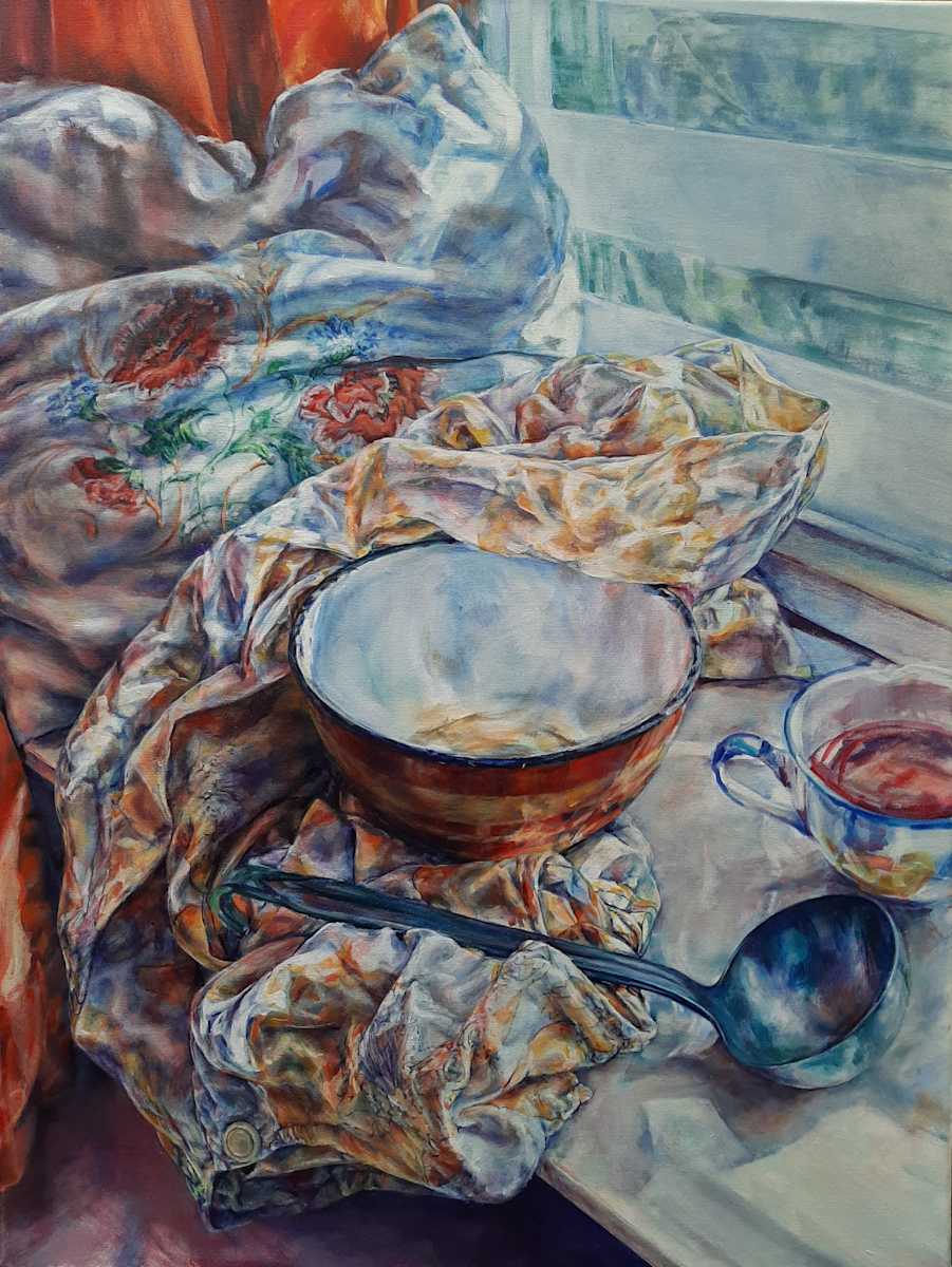 Just a spoonful by Agnes Havran  Image: Amid the folds of a soft cushion, an embroidered floral detail emerges, encouraging a closer look and grounding this scene of quiet domesticity. This gentle, introspective still life subtly challenges the viewer’s expectation of order with its artful arrangement. The rich, earthy tones of an enamel bowl rest upon a crumpled apron, their textures offering a tactile contrast to the smooth ceramic cup nearby. What does this combination of form and material suggest about the spaces we inhabit? The serene tableau envelops the viewer in a cozy setting, where each sensory layer—from the warmth of colours to the gentle light filtering in—creates a space for peaceful introspection.