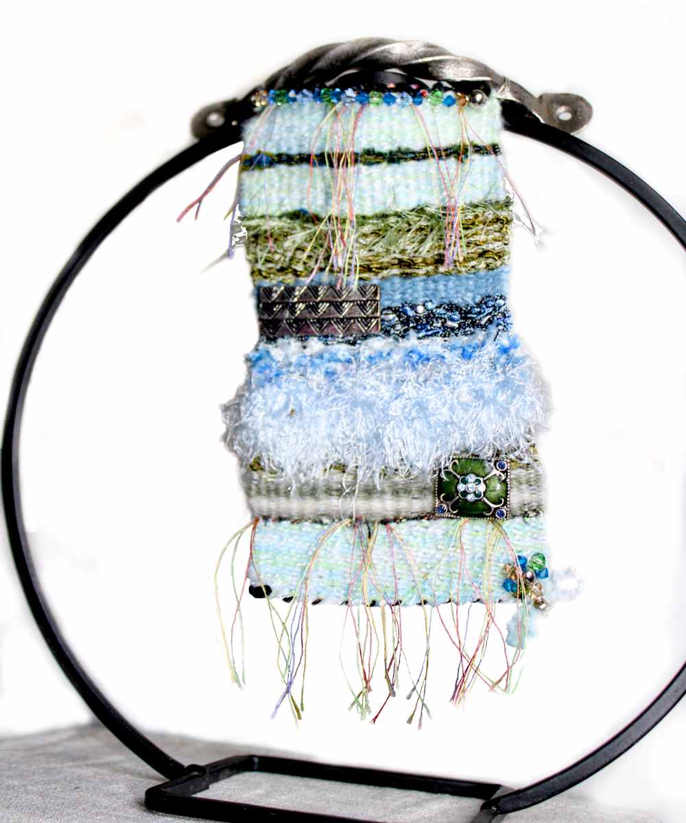 Tranquil Balance Mini Art Tapestry by Annette  Image: Unique circle ornament hanger (does not come with artwork) showcases this one of a kind mini art tapestry made with unique yarns. You will find colorful string,  soft eyelash, ladder, cotton and more with beautiful crystals and accent jewelry make this a true collectable piece. 