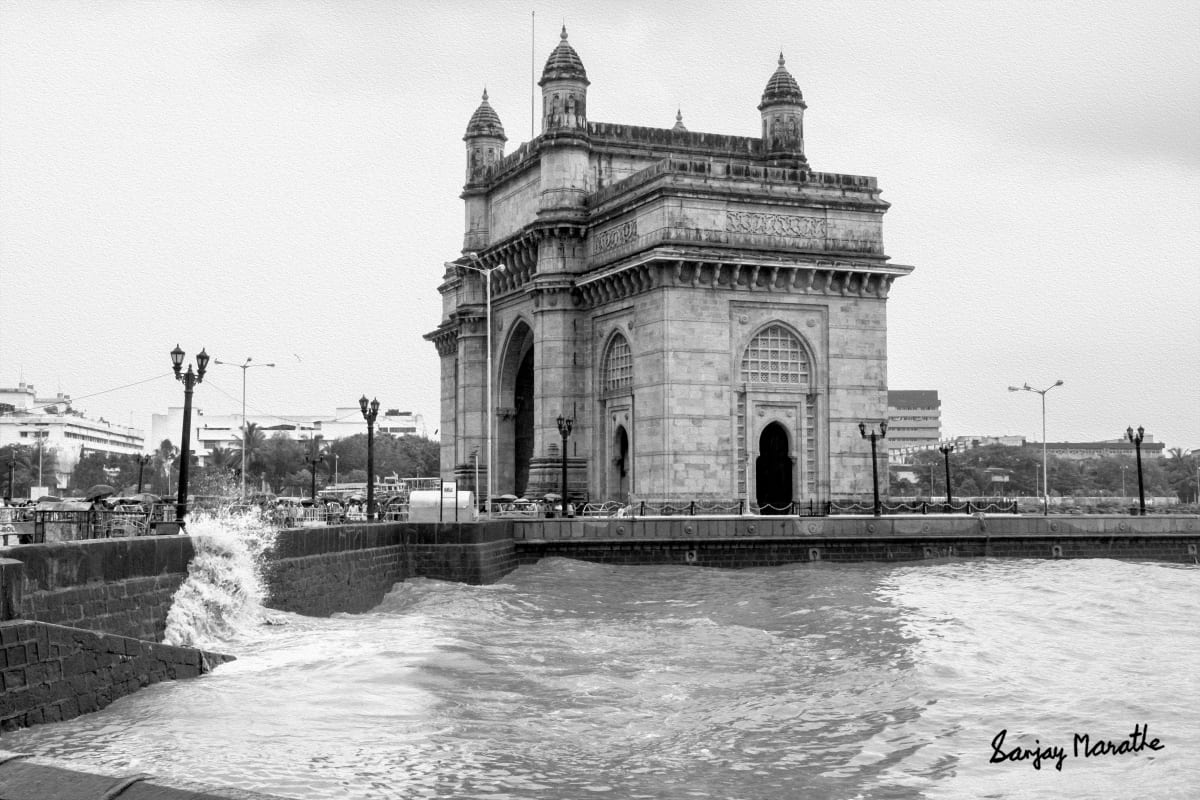 Gateway Of India, Mumbai (2013) by Sanjay Marathe  Image: A nostalgic black and white photograph of the Gateway of India. A monsoon wave in the swelled Arabian sea splashes on the stone embankment.                                                            

The Gateway of India was built to commemorate the visit of King George V and Queen Mary to Mumbai (then Bombay) in 1924 CE, designed as a grand ceremonial entrance to the city and became one of Mumbai's most iconic landmarks.
