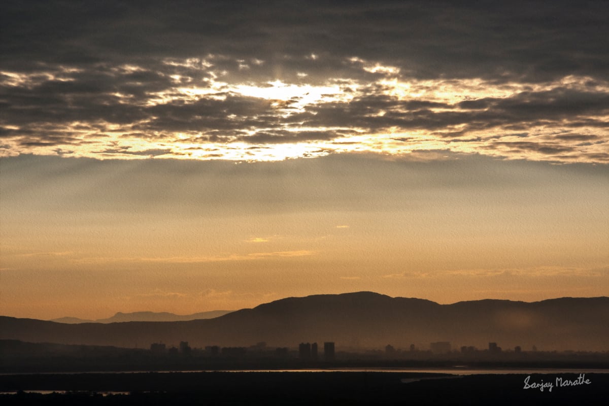 Gold Shimmer, Navi Mumbai Landscape by Sanjay Marathe  Image: On a misty winter morning, just as the sun began to pierce through the dark clouds, I captured the golden shimmer illuminating the scene. In the distance, the New Mumbai hill range and the Ghansoli buildings rise beyond the glistening creek in the foreground, evoking the aura of a long-lost city.
