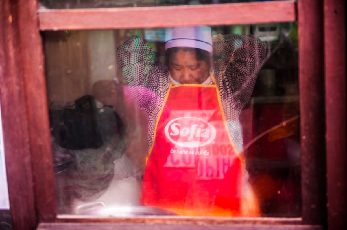 Untitled (Carmen Rosa at  her restaurant, through the window)  Image: Carmen Rosa, the founder of the group "Las Diosas del Ring", pioneer and champion of lucha, working in a restaurant snack bar in the city center of La Paz.